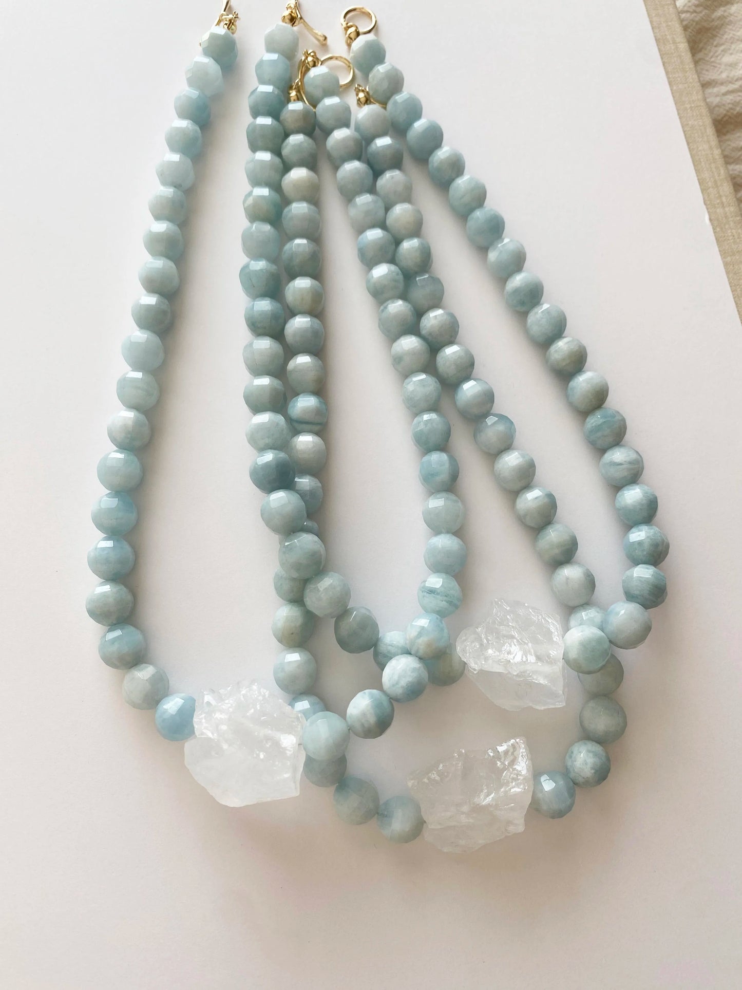 Two light blue beaded Aquamarine necklaces with gold clasps on a white surface.