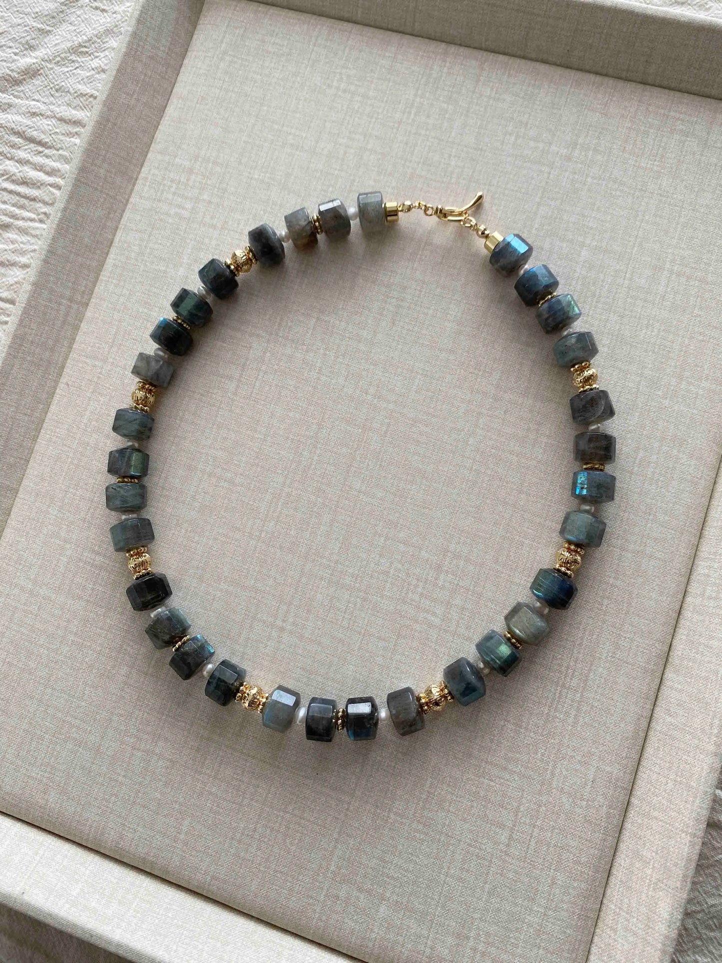 Labradorite Necklace with gray beads and gold accents on a beige fabric background