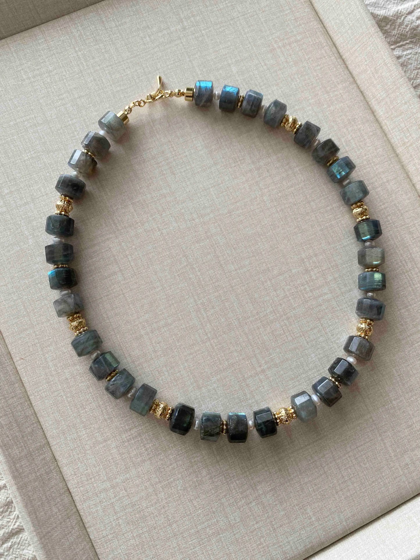Labradorite Necklace with blue and gold beads on a beige fabric background