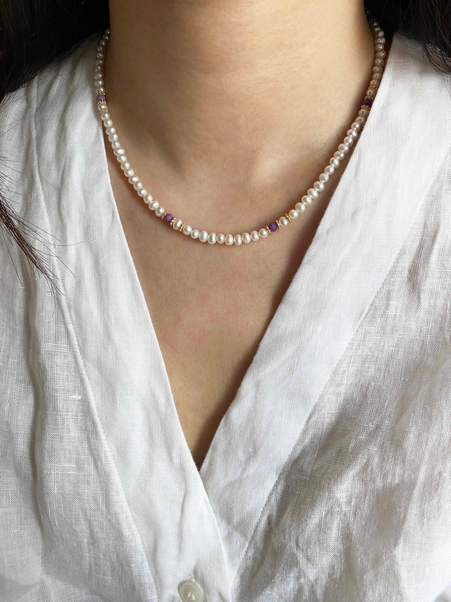 Pearl necklace with purple stones worn by a person in a white shirt