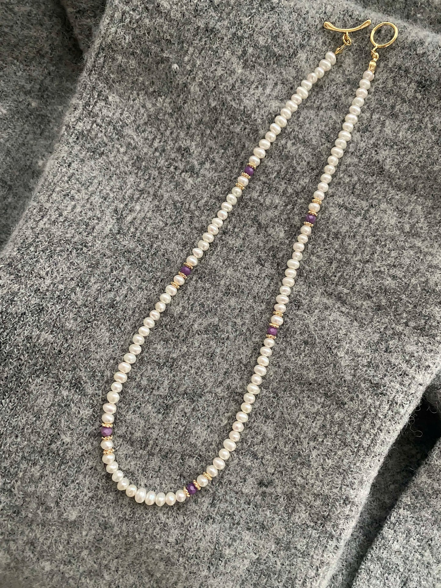 Lepidolite Pearl necklace with gold clasp on a textured gray surface