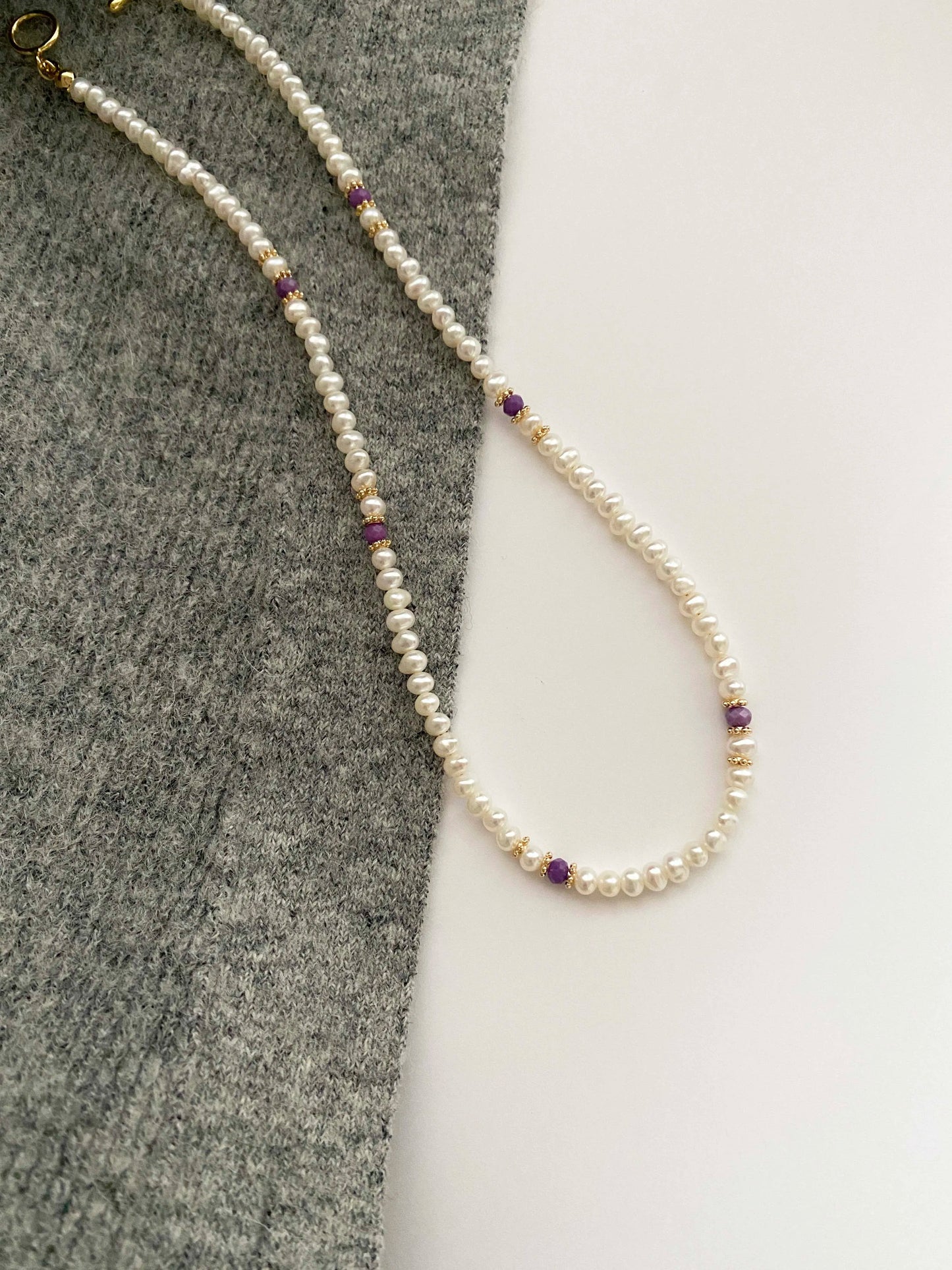 Pearl necklace with purple beads on a gray and white background