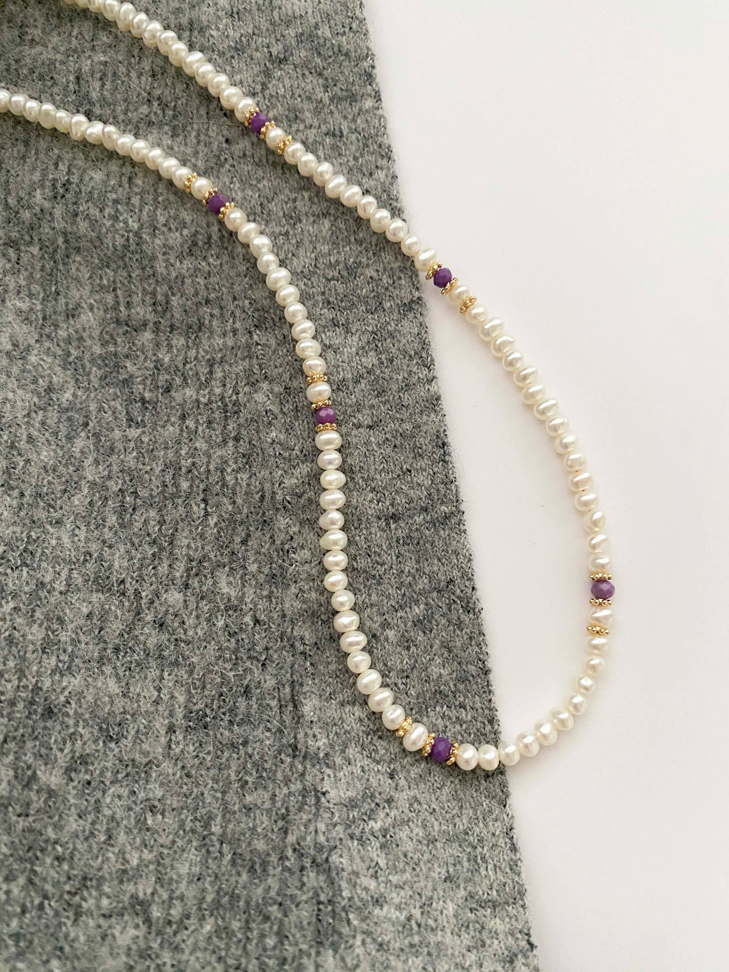 Pearl necklace with small beads on a gray fabric background