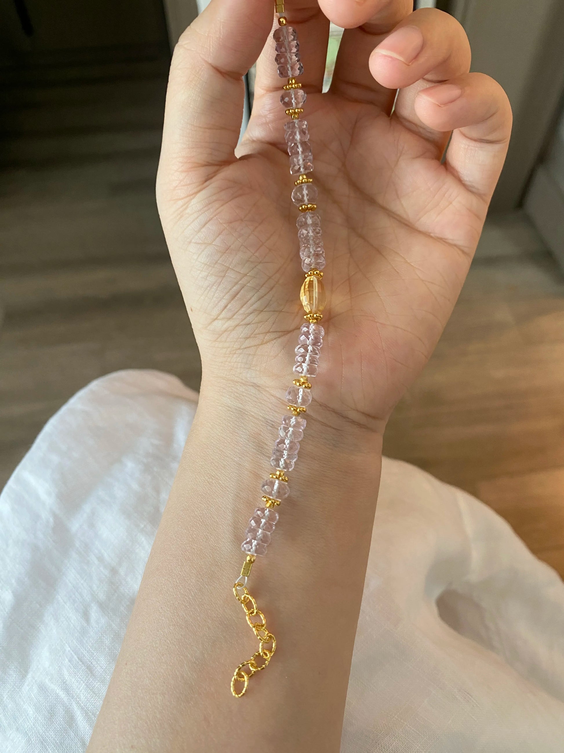 Hand holding a beaded bracelet with gold accents on a neutral background