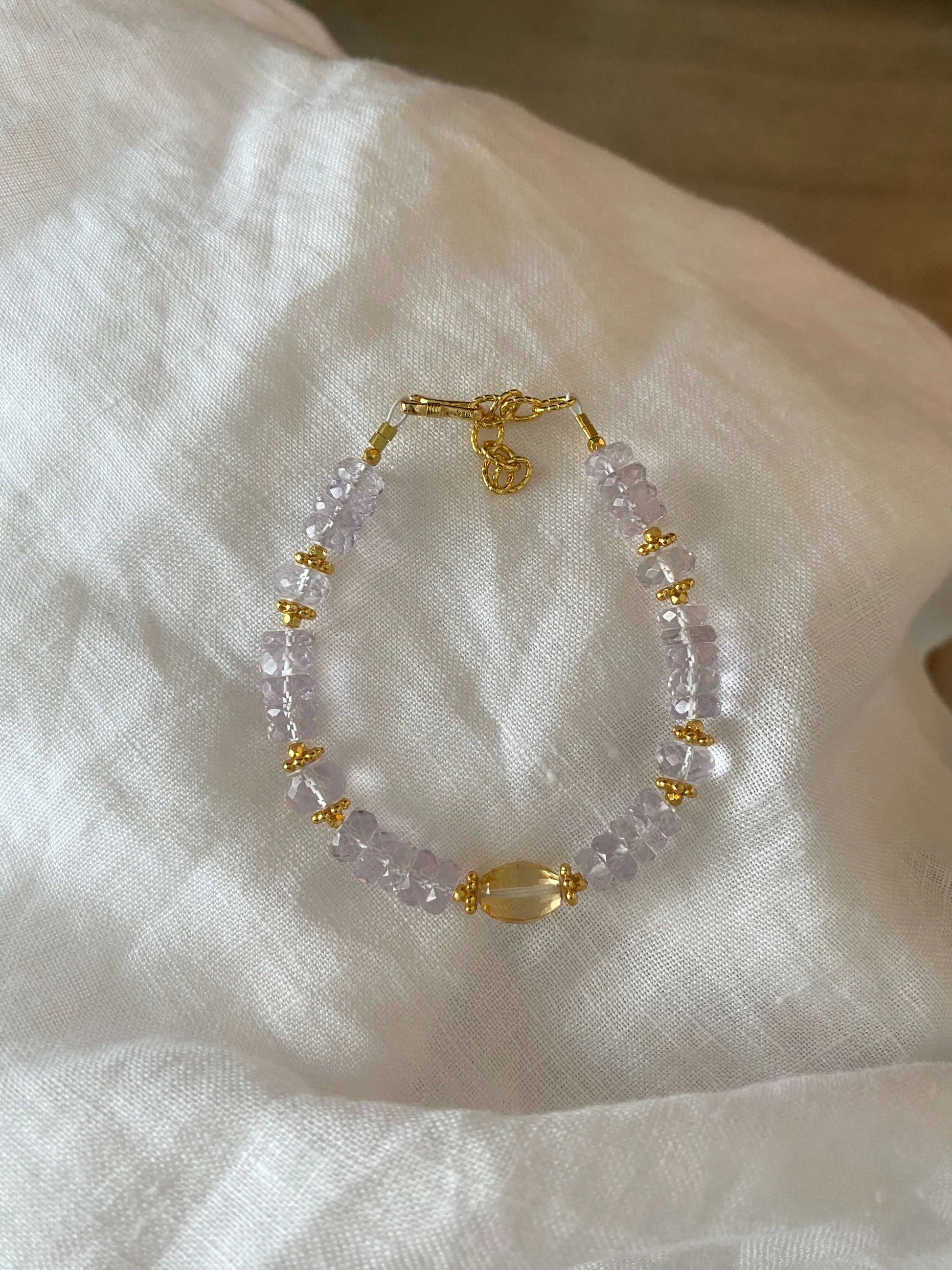 Bracelet with 5A Amethyst purple beads and gold accents on a white fabric background