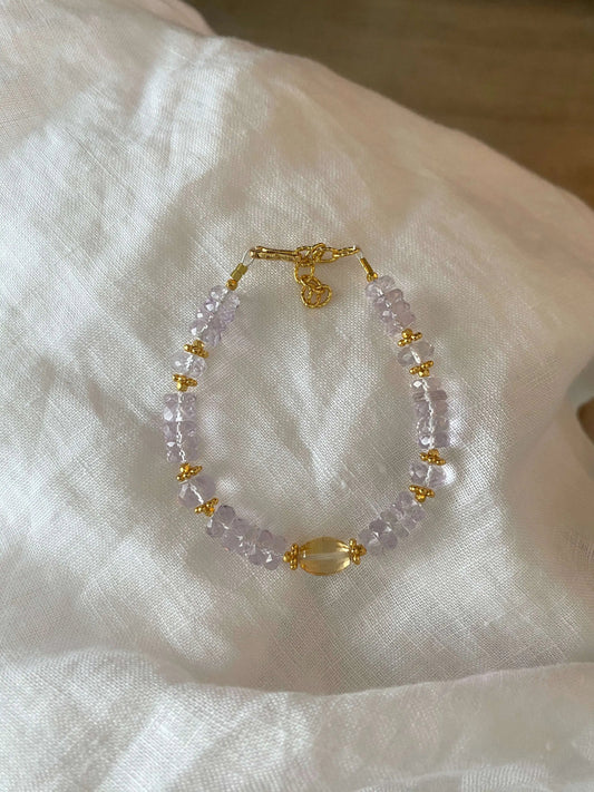 Bracelet with 5A Amethyst purple beads and gold accents on a white fabric background