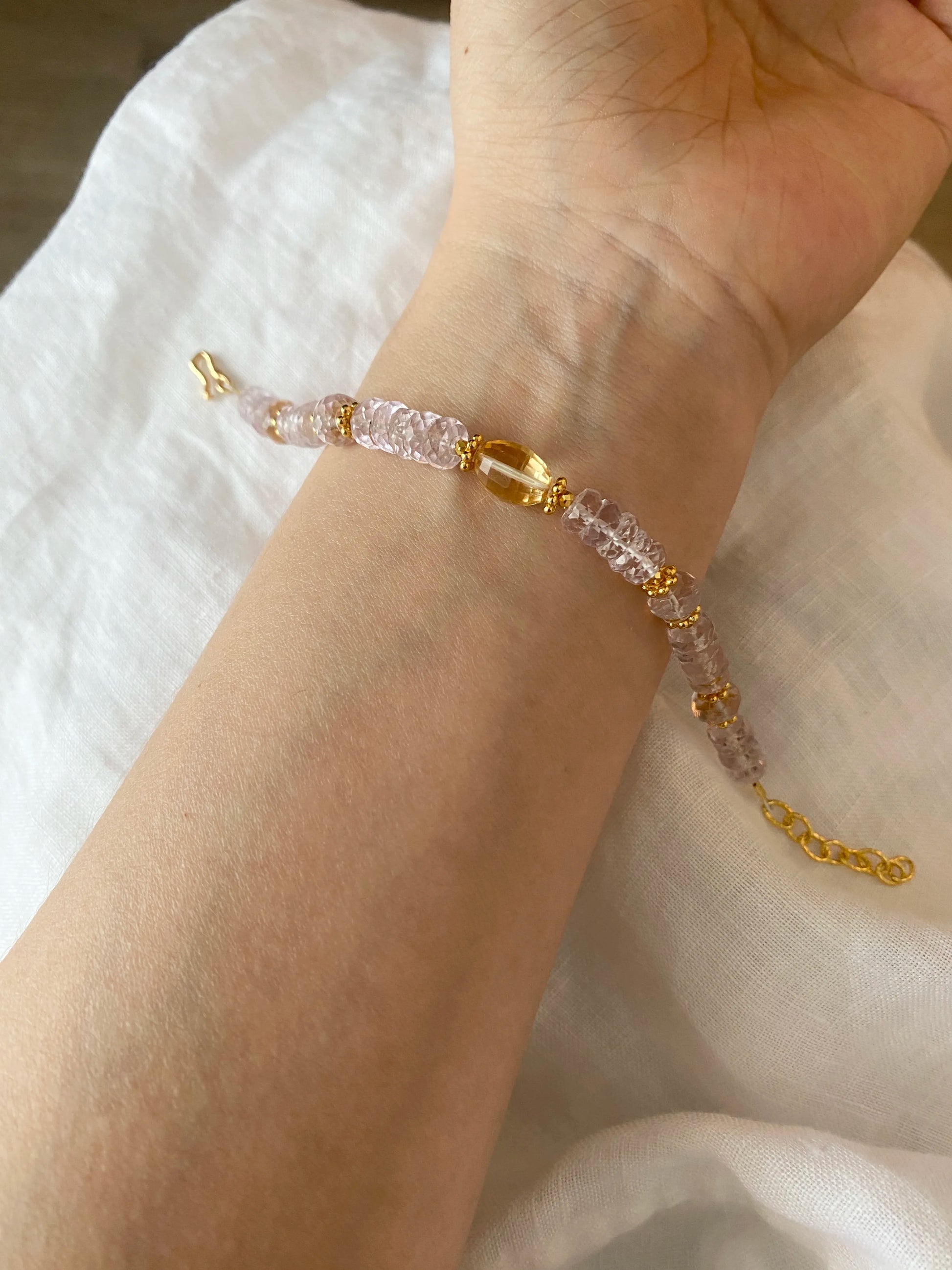 Bracelet with pink and gold beads on a wrist against a white fabric background