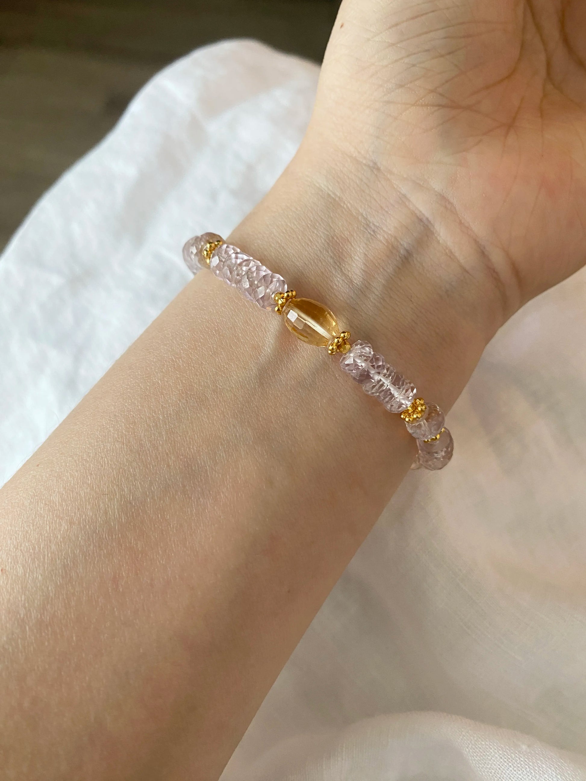 Bracelet with 5A Amethyst pink and gold beads on a wrist against a neutral background