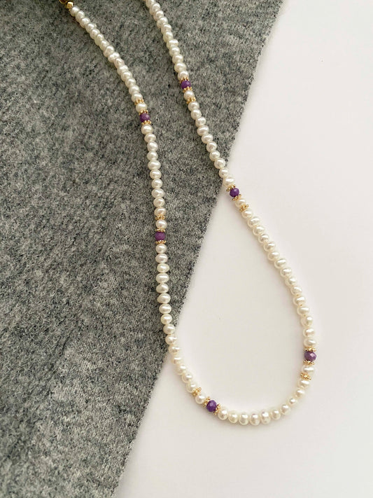 Pearl necklace with purple beads on a gray and white background